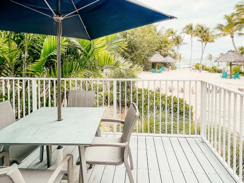 a table and chairs on a deck with a beach and trees