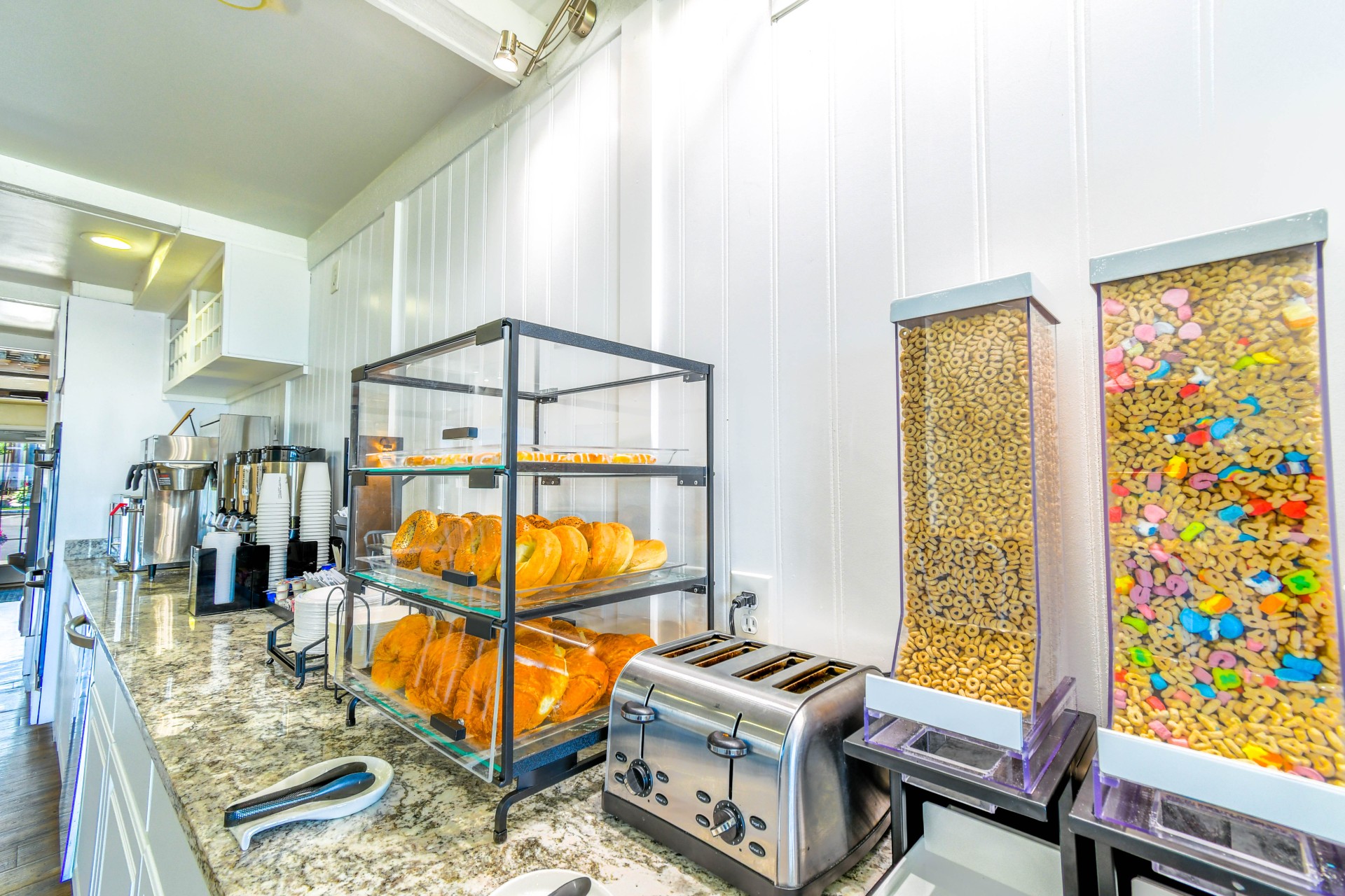 A breakfast buffet with pastries, cereal dispensers, and a toaster.