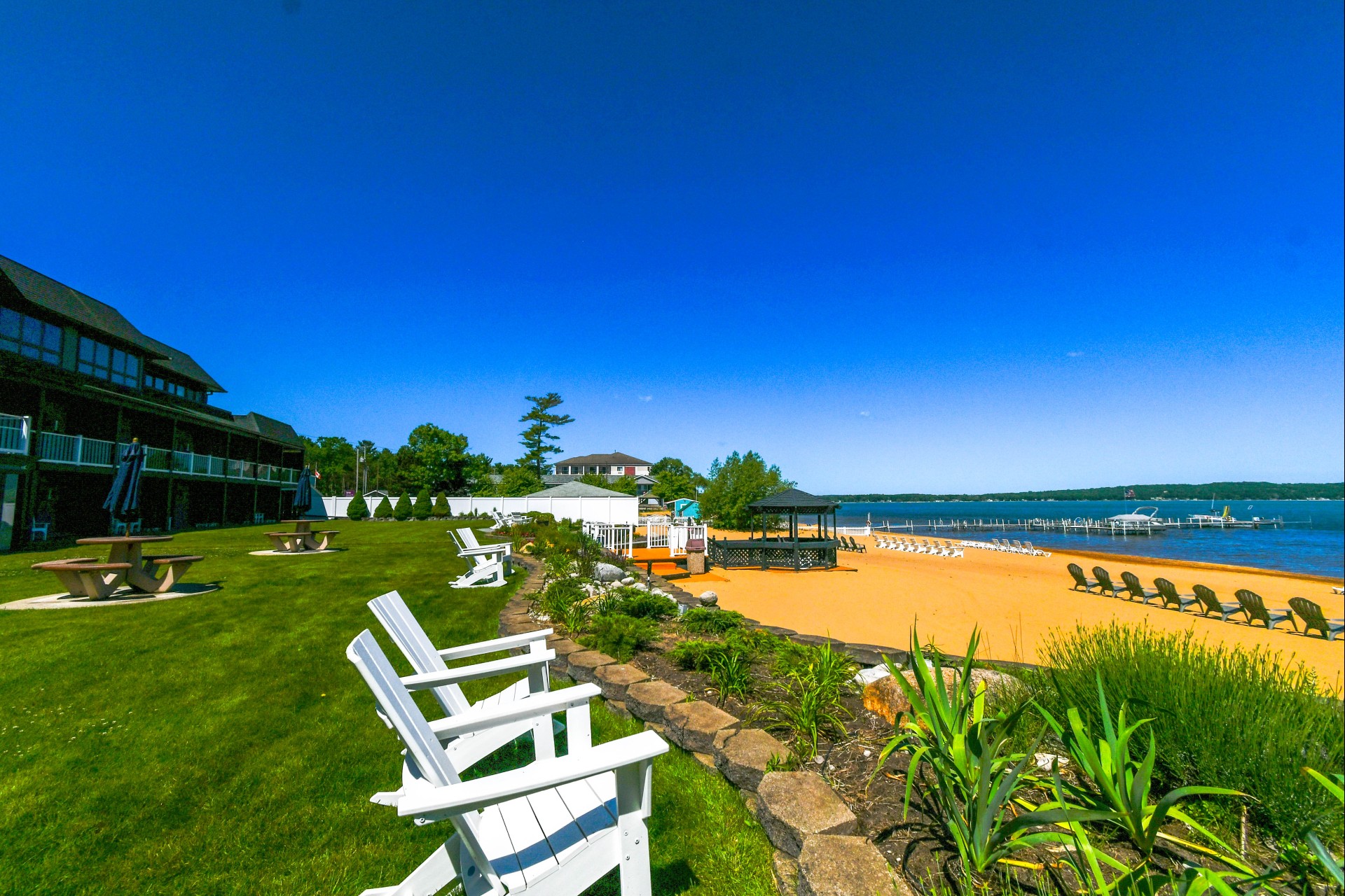 A beachside view of a hotel with a large lawn, seating areas, and a pier extending into the water.