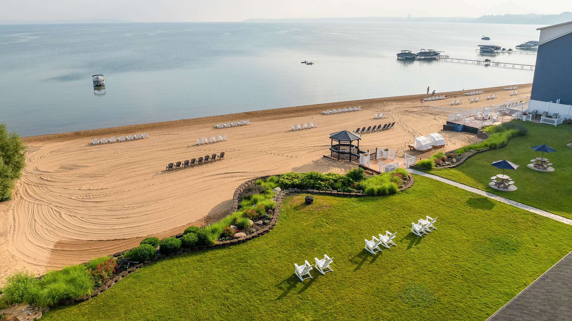 Aerial view of a beach with a lawn, pier, and gazebo.