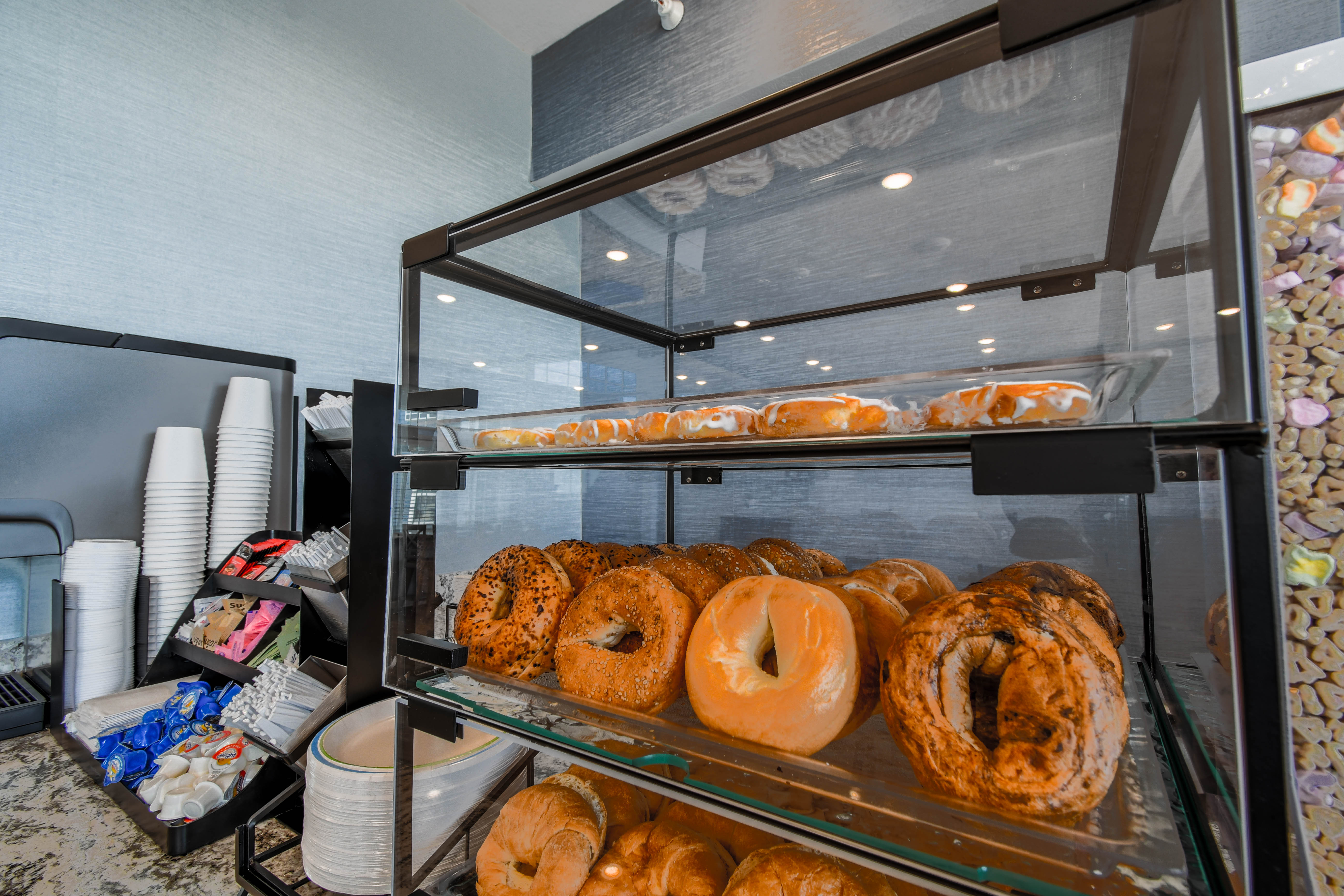 A display case filled with pastries and a beverage station with cups and creamers.