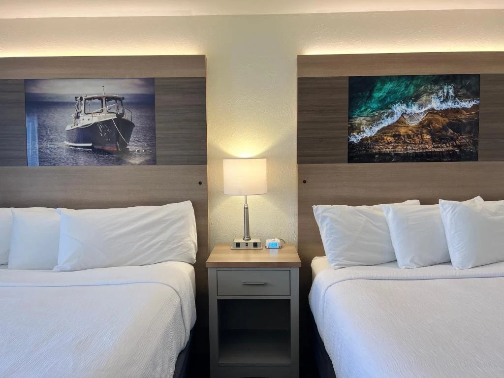 two beds with white sheets and a lamp on a nightstand