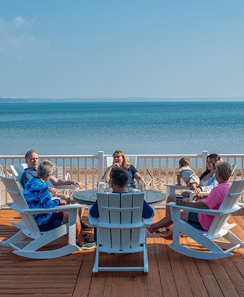 a group of people sitting around a table on a deck overlooking the ocean