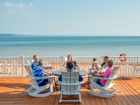 a group of people sitting around a table on a deck overlooking the ocean