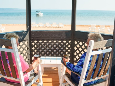 a couple of men sitting on a deck with chairs and a boat in the background