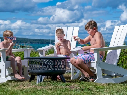 a group of boys sitting in chairs outside by a fire pit