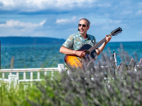 a man playing guitar on a fence by the water