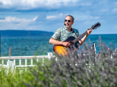 a man playing guitar on a fence by the water