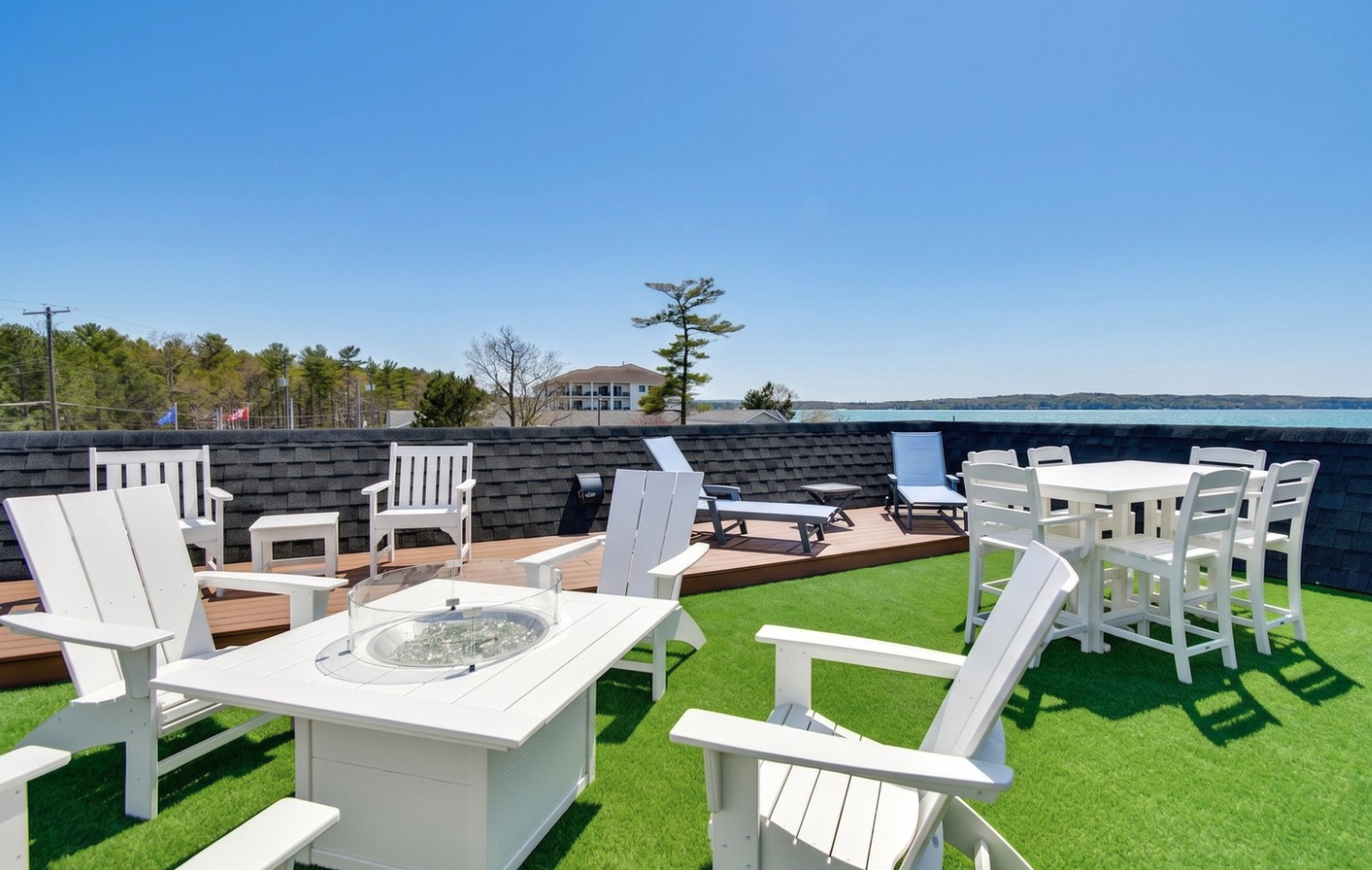 a patio with white chairs and a fire pit on a green lawn
