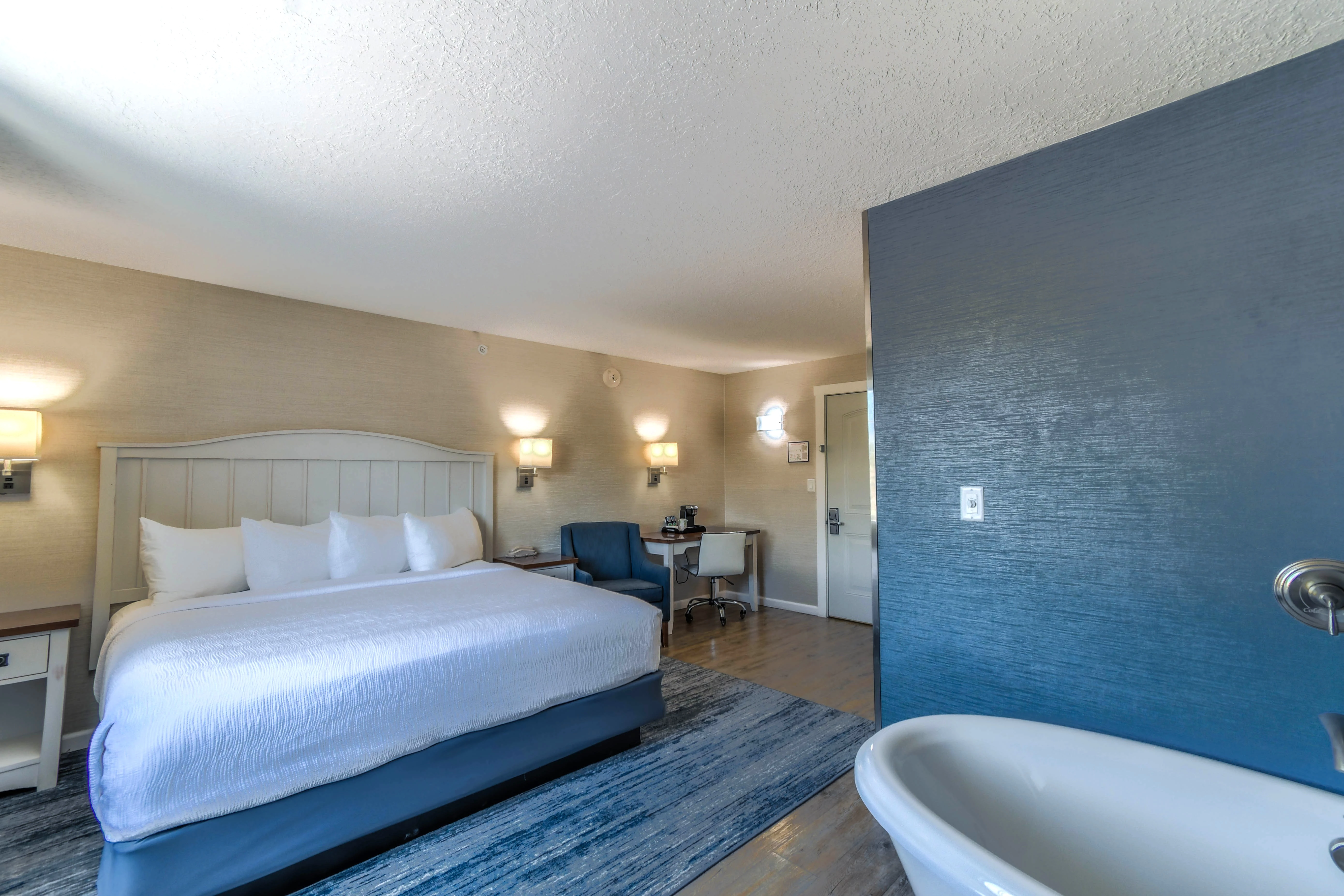 A hotel room with a bed, desk, chair, and bathroom.