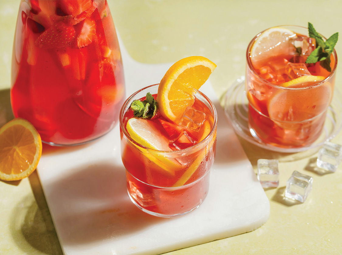 a glass of red liquid with orange slices and ice