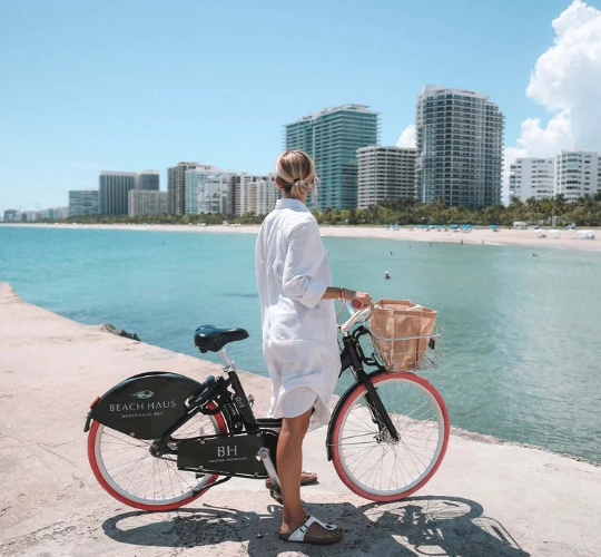 a woman standing on a sidewalk with a bicycle by the water