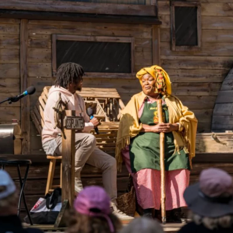 a woman holding a stick and a man sitting on a stage