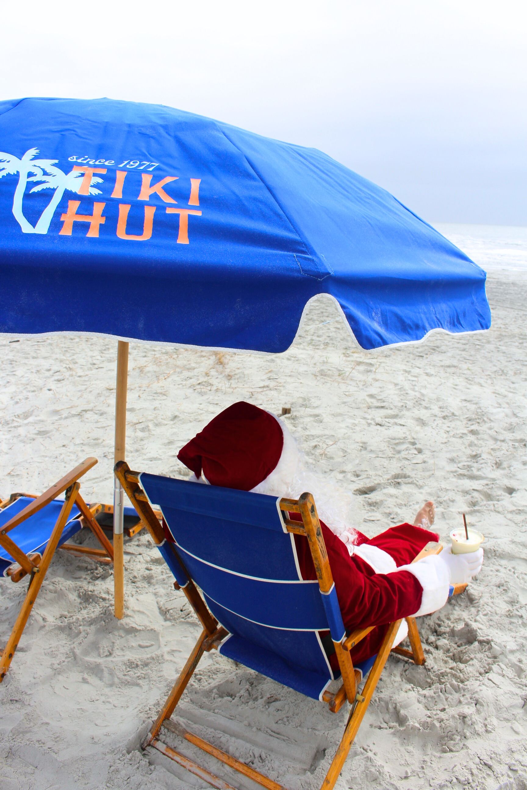 a person in a santa garment sitting in a chair under an umbrella on a beach