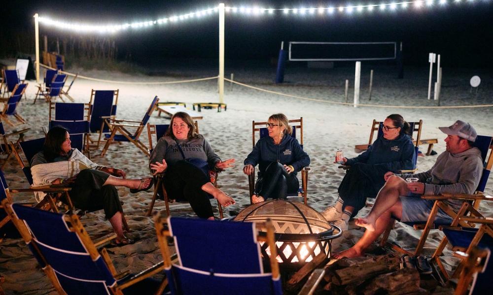 a group of people sitting around a fire pit on a beach
