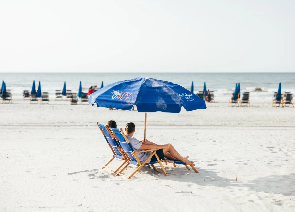 a man and woman sitting under a blue umbrella on a beach