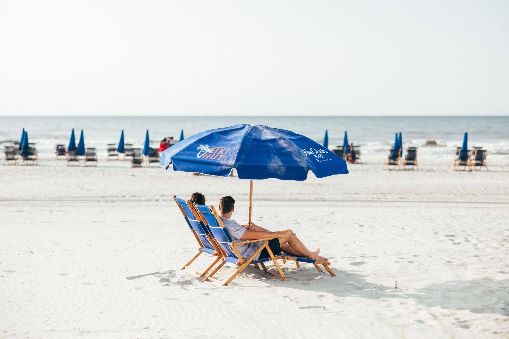 a couple sitting under a blue umbrella on a beach