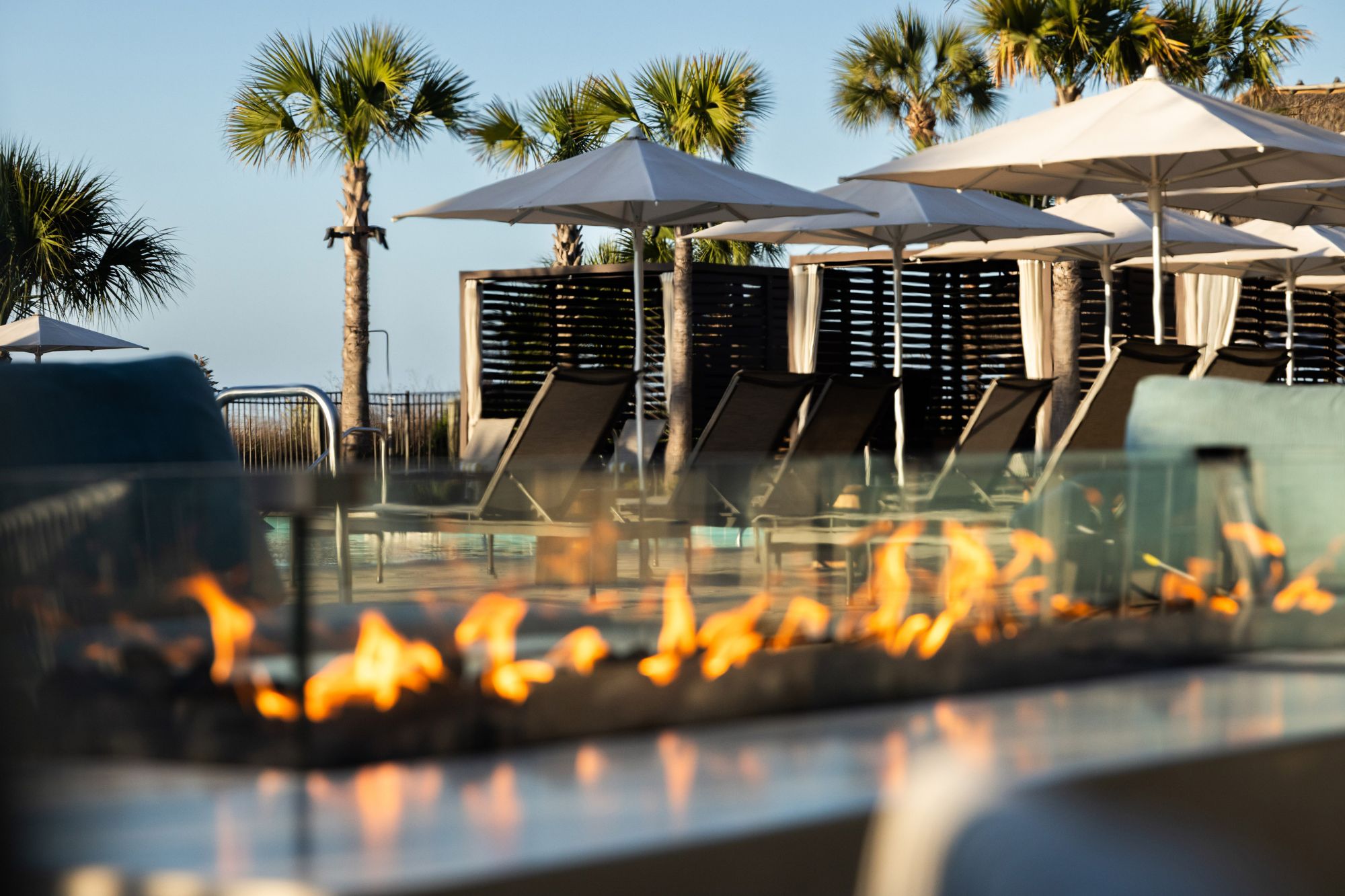 a fire pit with chairs and umbrellas by a pool