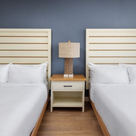 two beds with white sheets and a lamp on a nightstand