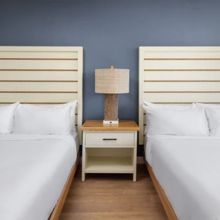 two beds with white sheets and a lamp on a nightstand
