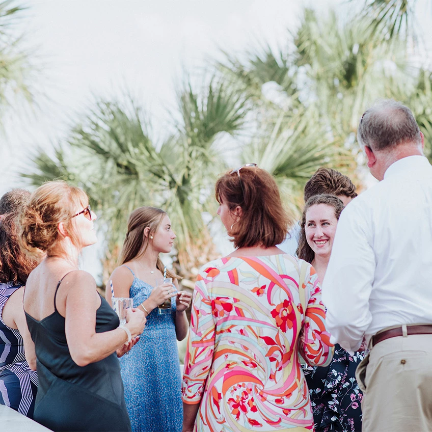a group of wedding guests talking outdoors with palm trees all around them