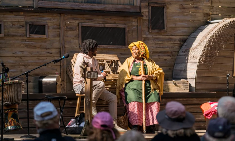 a woman holding a stick and a man sitting on a chair