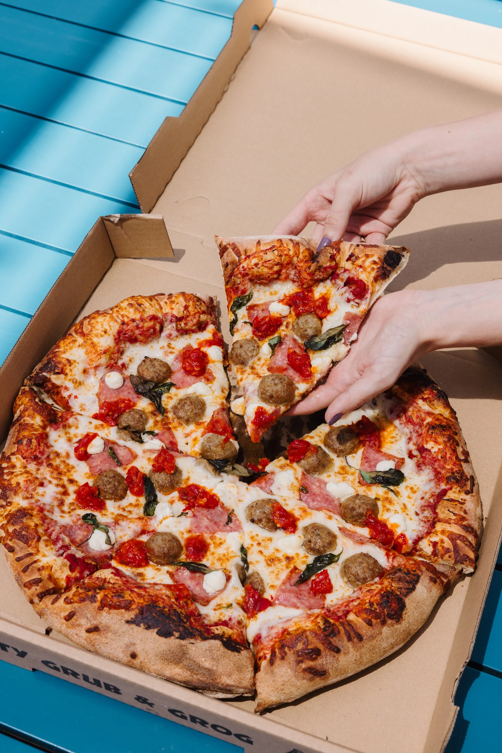 a person's hands taking a slice of pizza out of a box