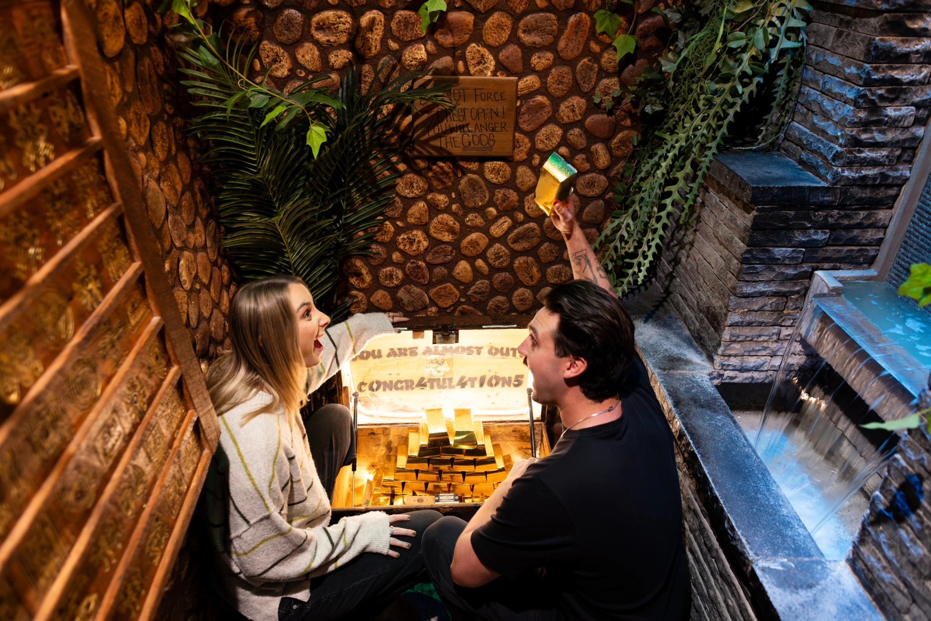 a man and woman sitting by a chest of gold in an escape room