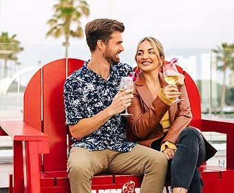 a man and woman sitting on a red bench holding drinks