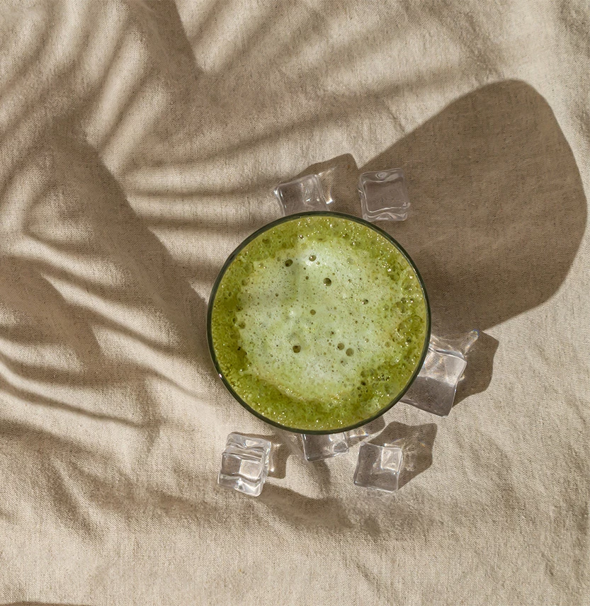 a glass of green drink with ice cubes on a white cloth