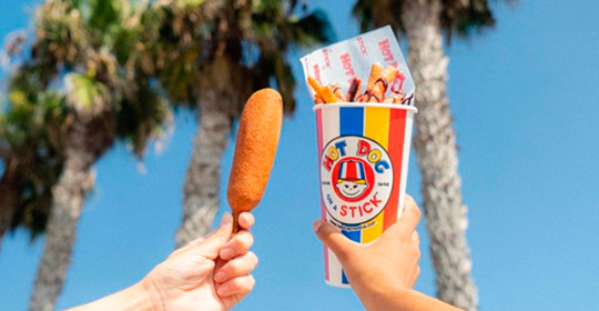 a hand holding a corn dog and a cup of fries