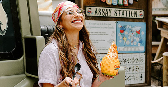 a woman smiling while holding a spoon and a pineapple ice cream