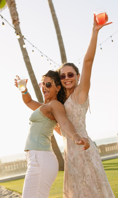 two women holding drinks and posing for the camera