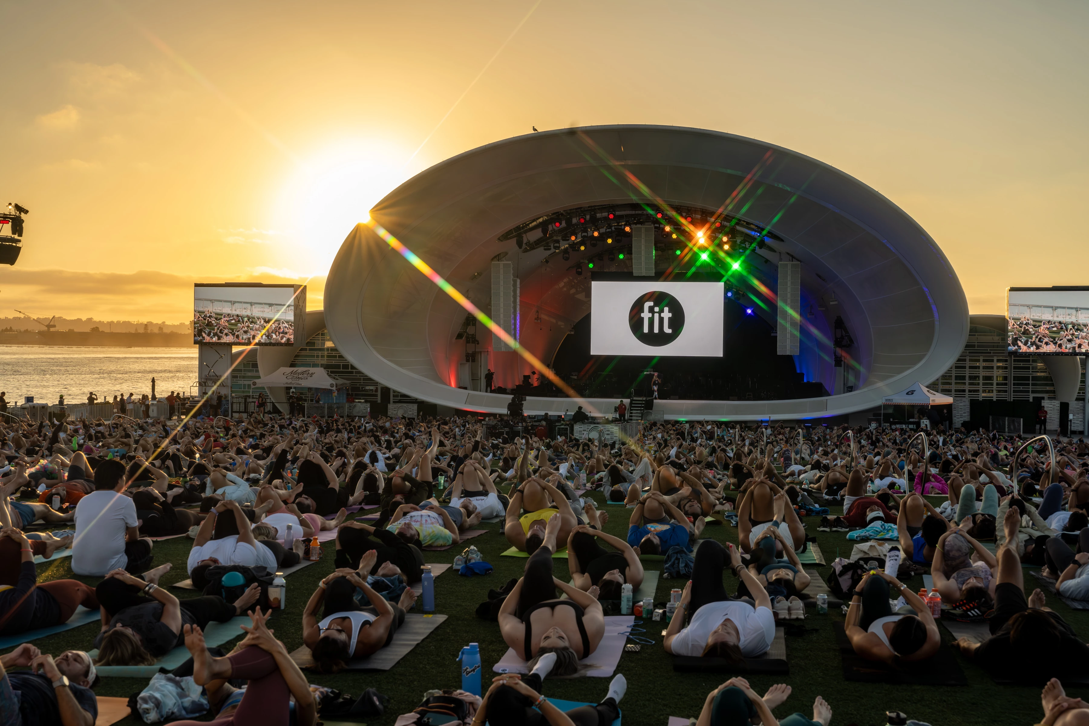 a large group of people sitting on the grass in front of a stage