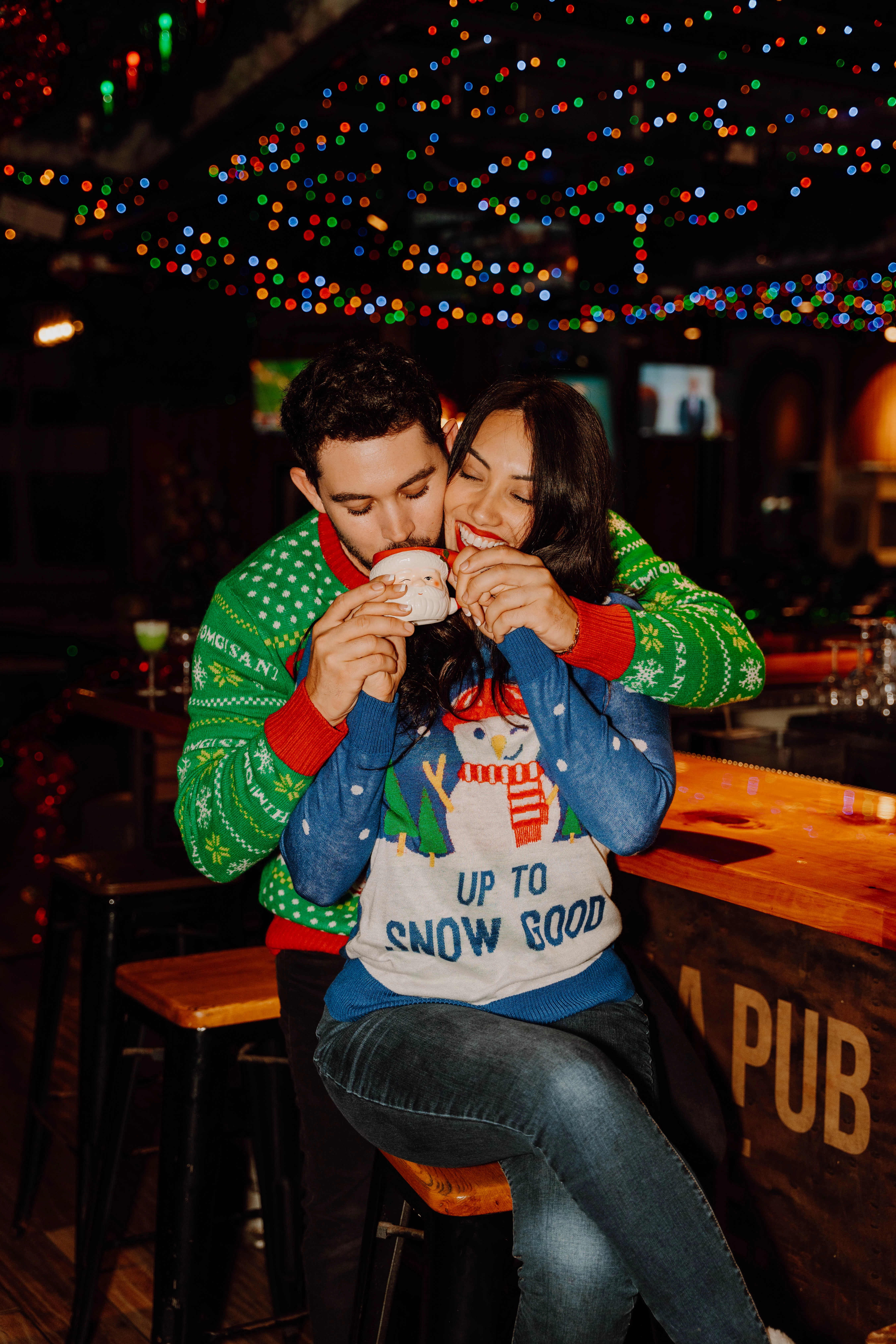 a man and woman sitting at a bar with christmas lights