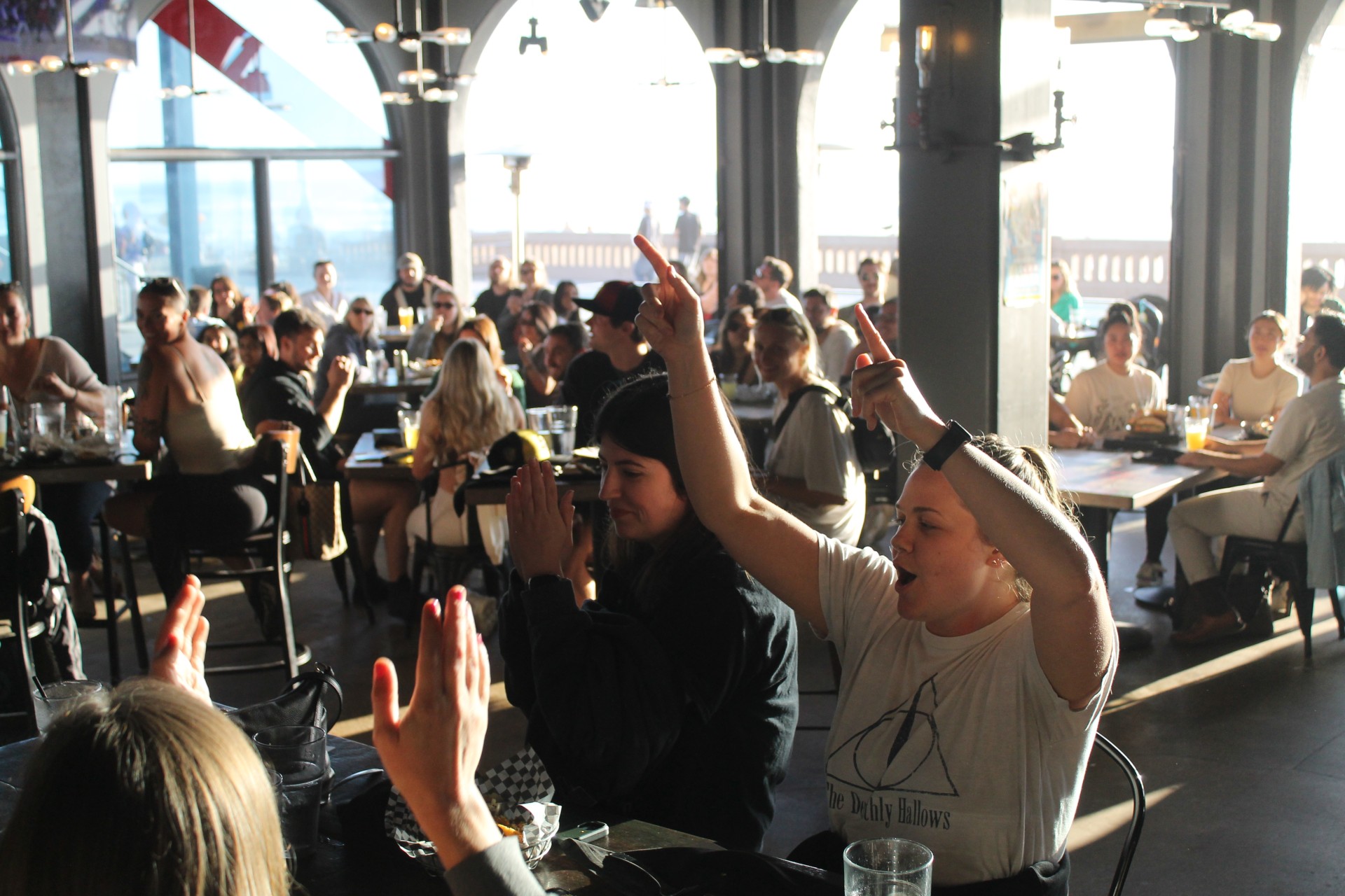 a group of people sitting at tables with their hands raised for a trivia question at Draft