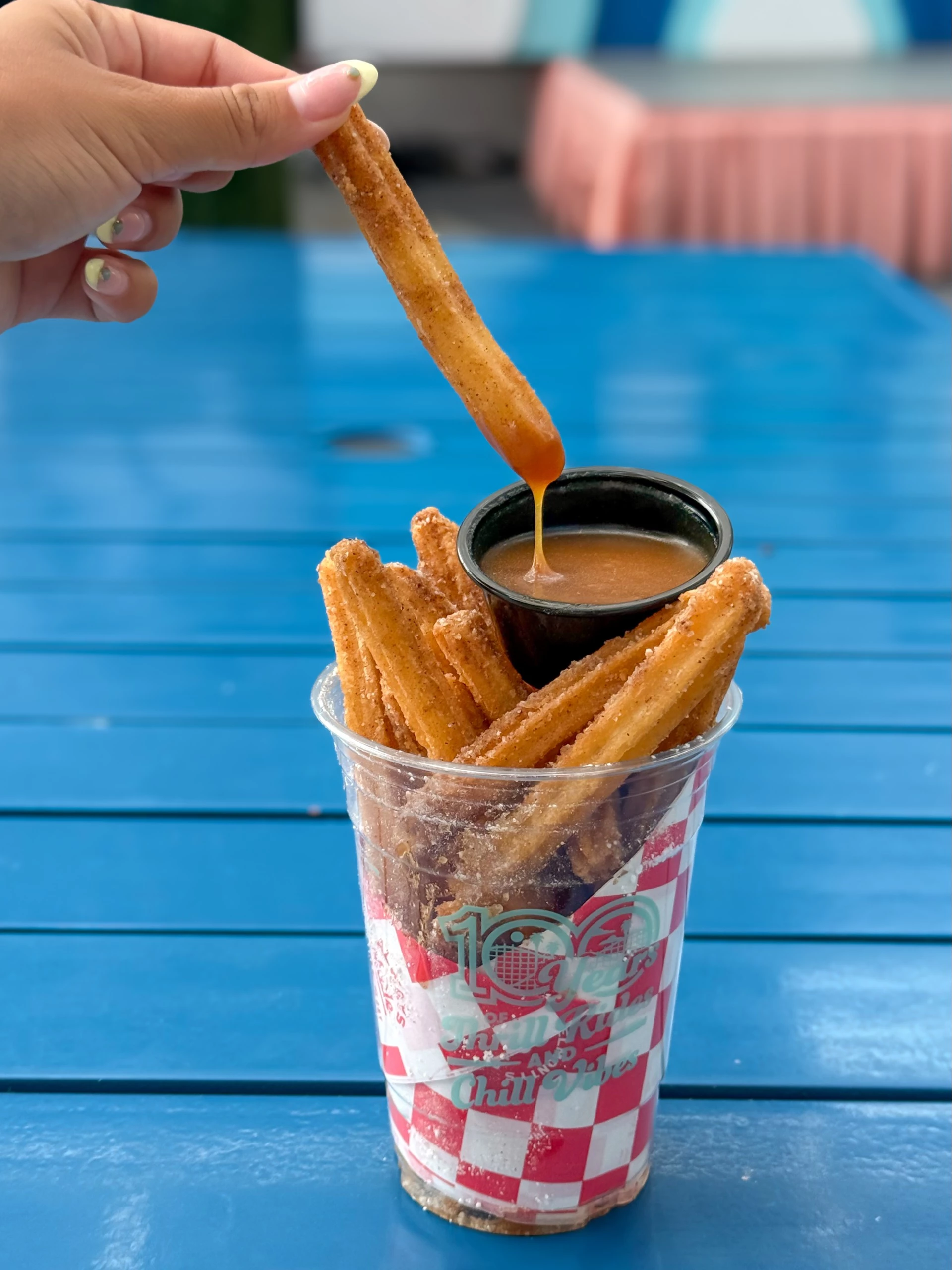 a hand holding a churro with sauce in a cup