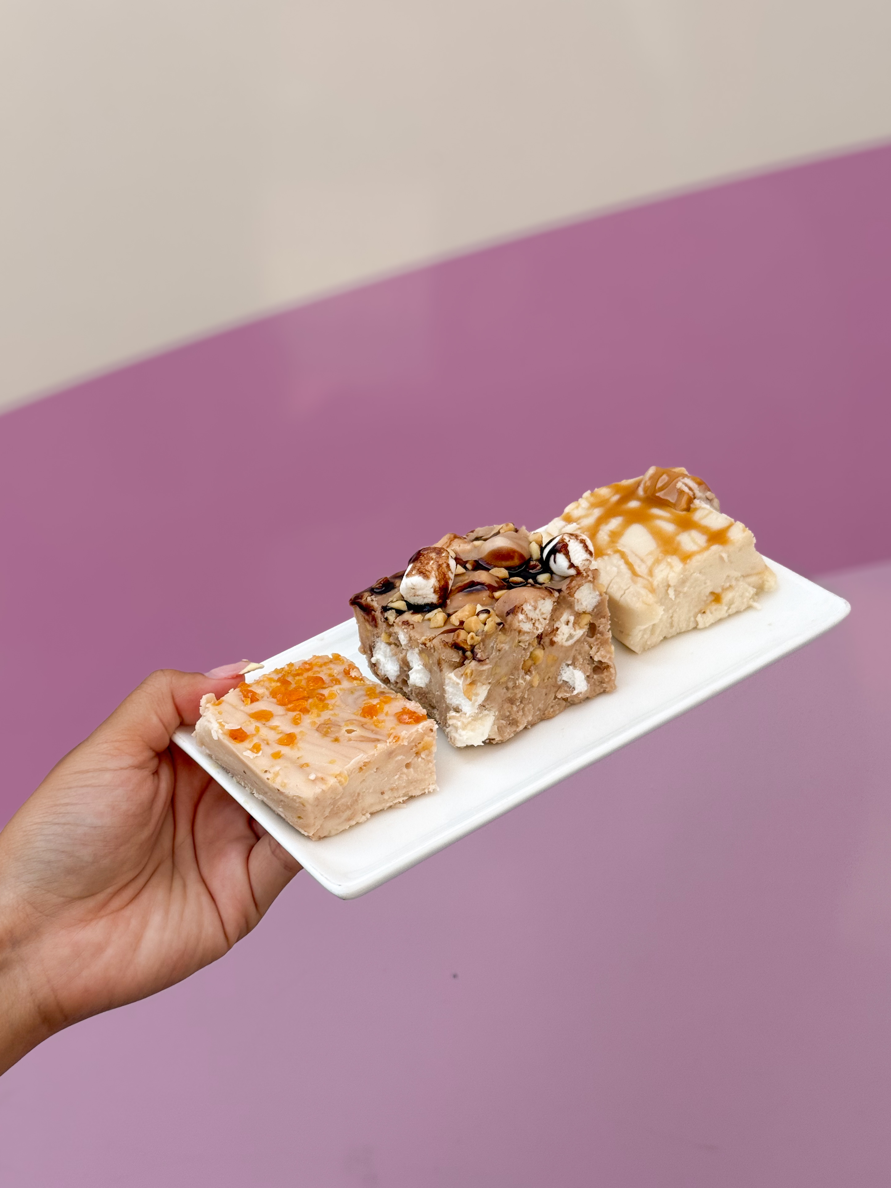 a hand holding a plate of three different fall-inspired fudge squares