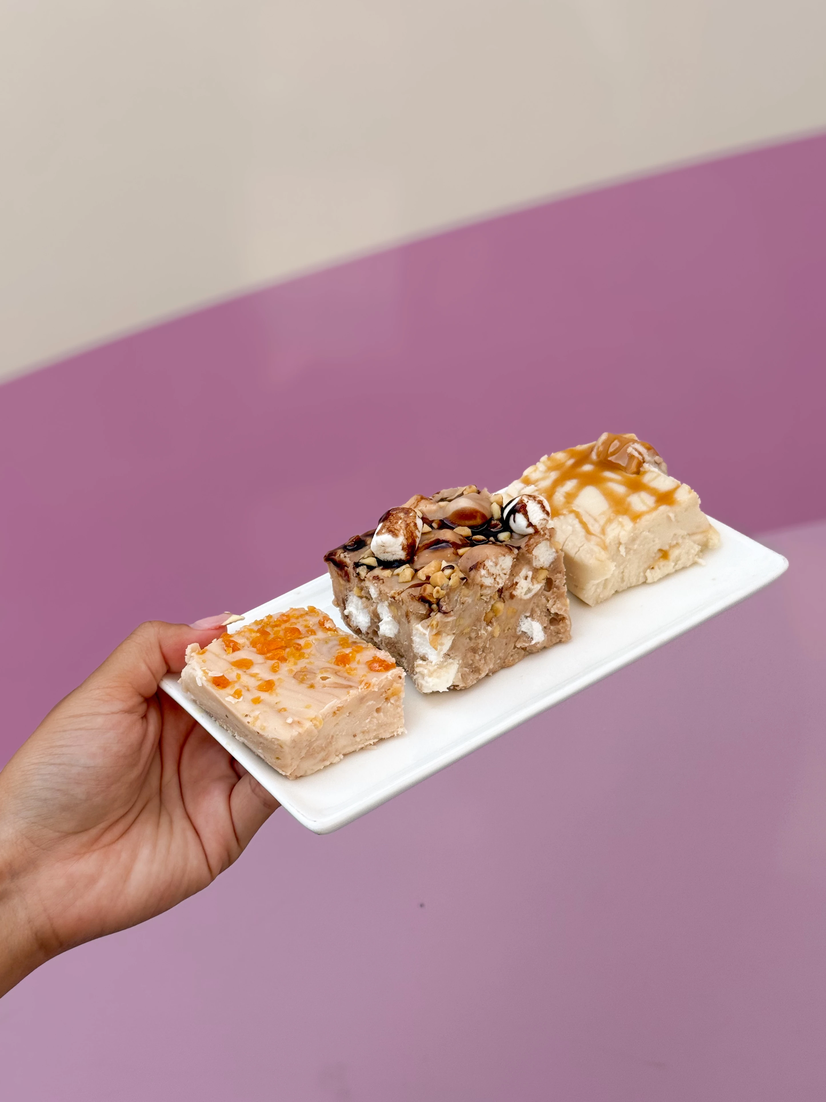 a hand holding a plate of three different fall-inspired fudge squares