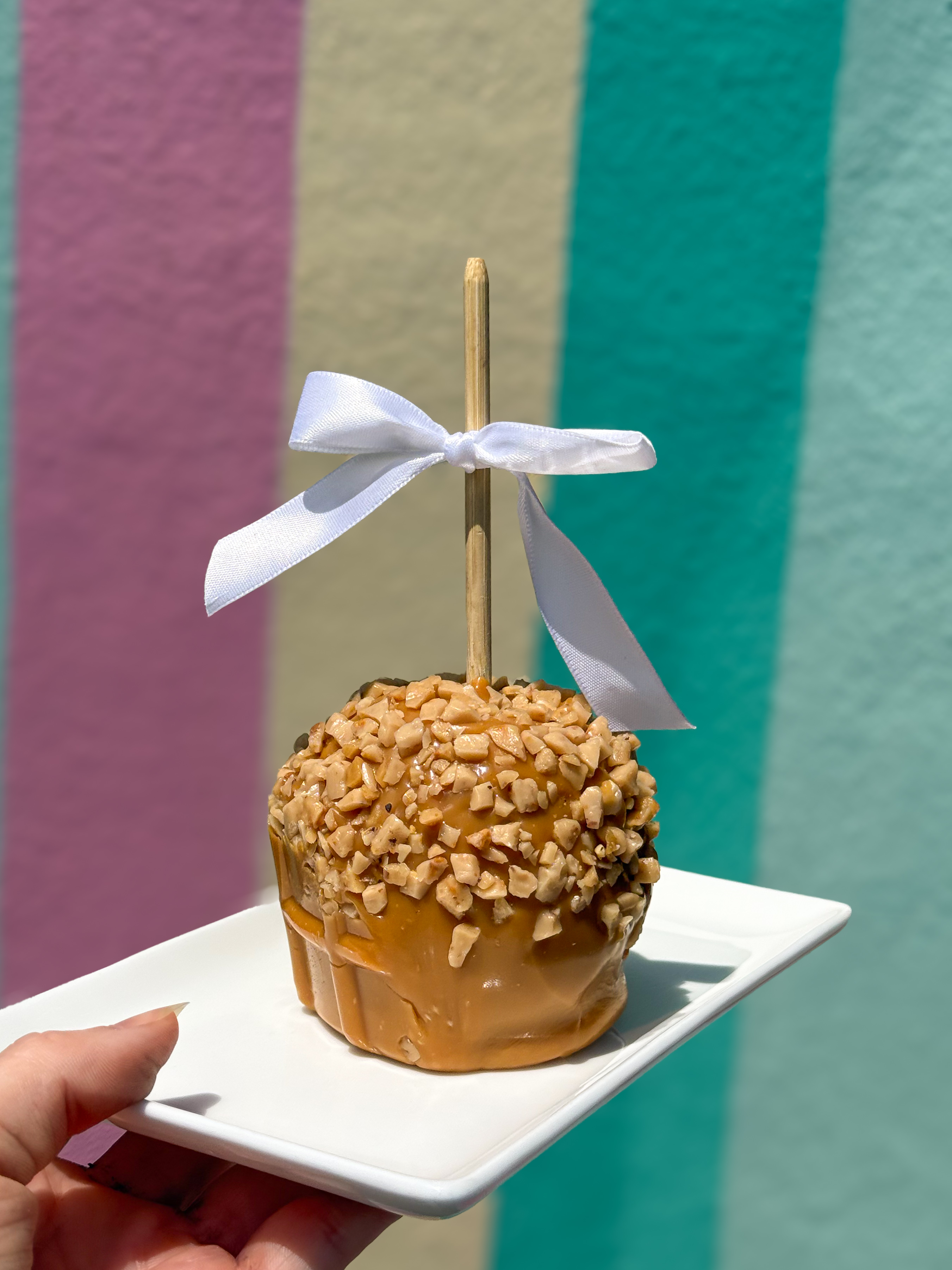 a hand holding a caramel apple with a white bow