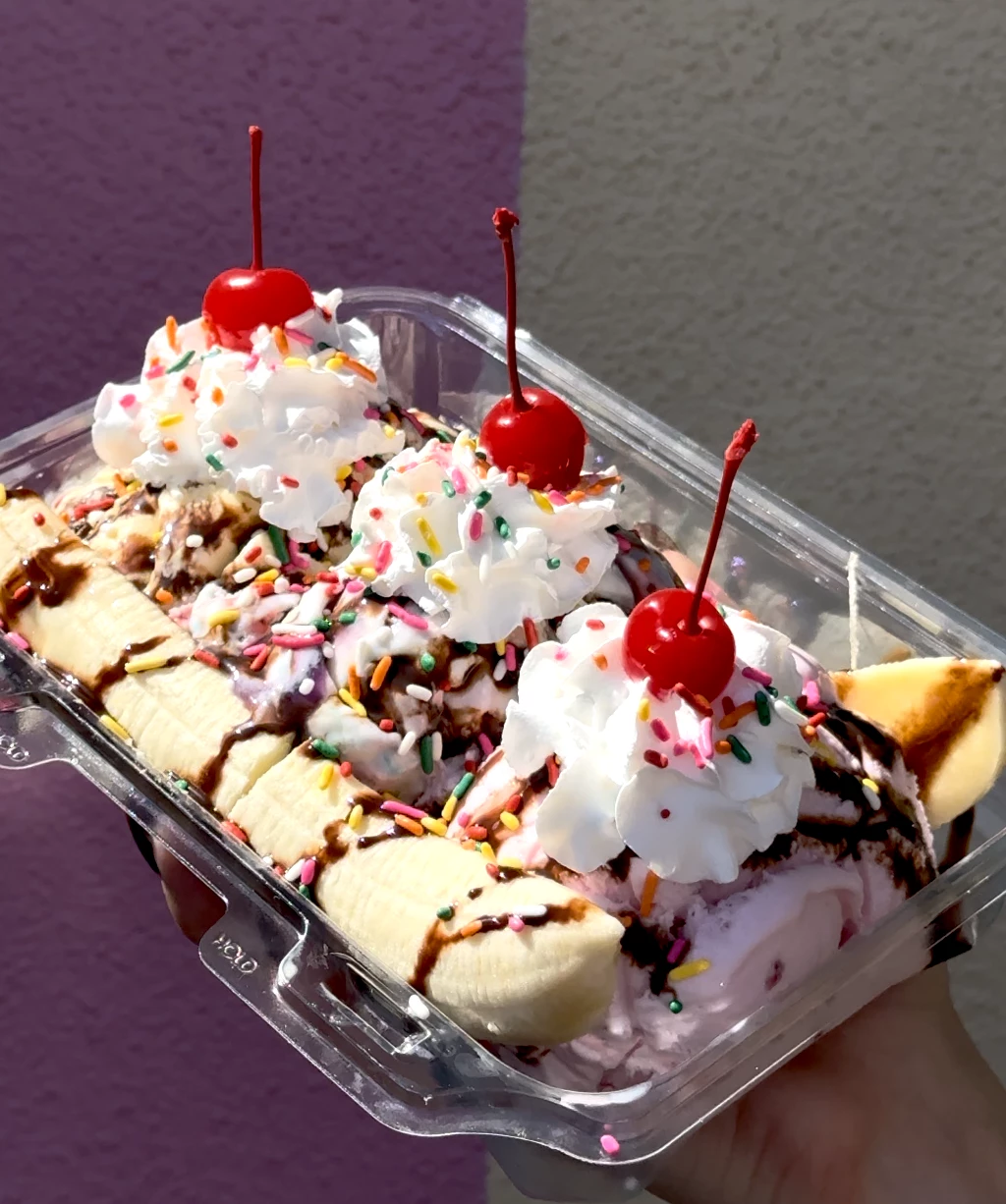 a plastic container of ice cream sundae with bananas and whipped cream and cherries
