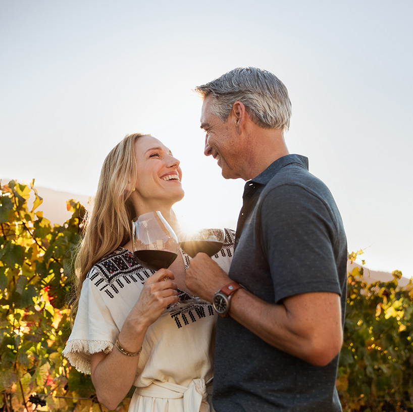 a man and woman holding wine glasses in a vineyard