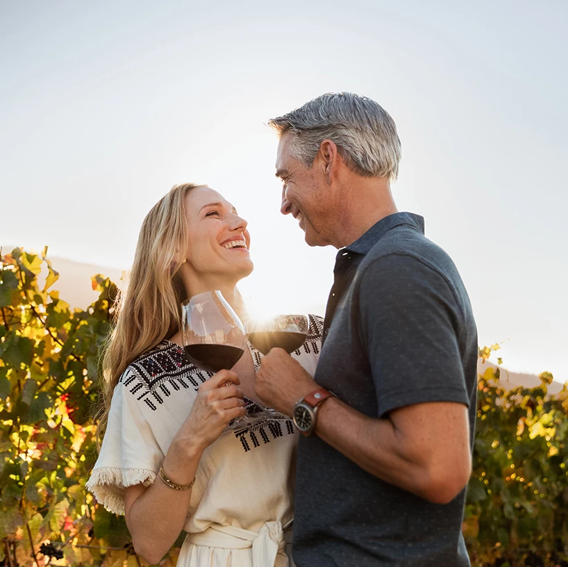 a man and woman holding wine glasses in a vineyard