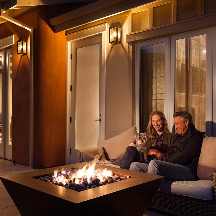 a man and woman sitting on a couch with a dog and a fire pit