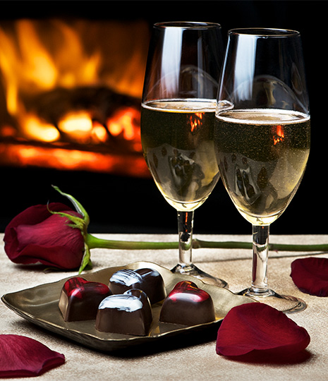 two glasses of wine next to a plate of chocolates and roses
