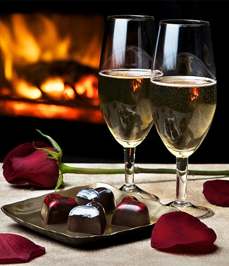 two glasses of wine next to a plate of chocolates and roses