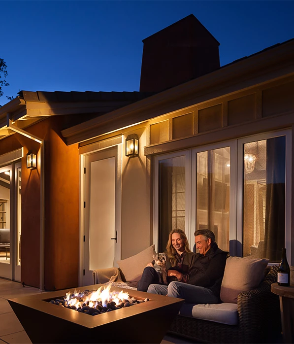 a man and woman sitting on a couch with a cat and a fire pit
