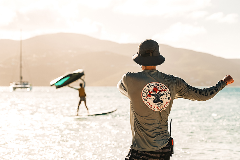 a man standing on a beach with a surfboard and a person on a surfboard