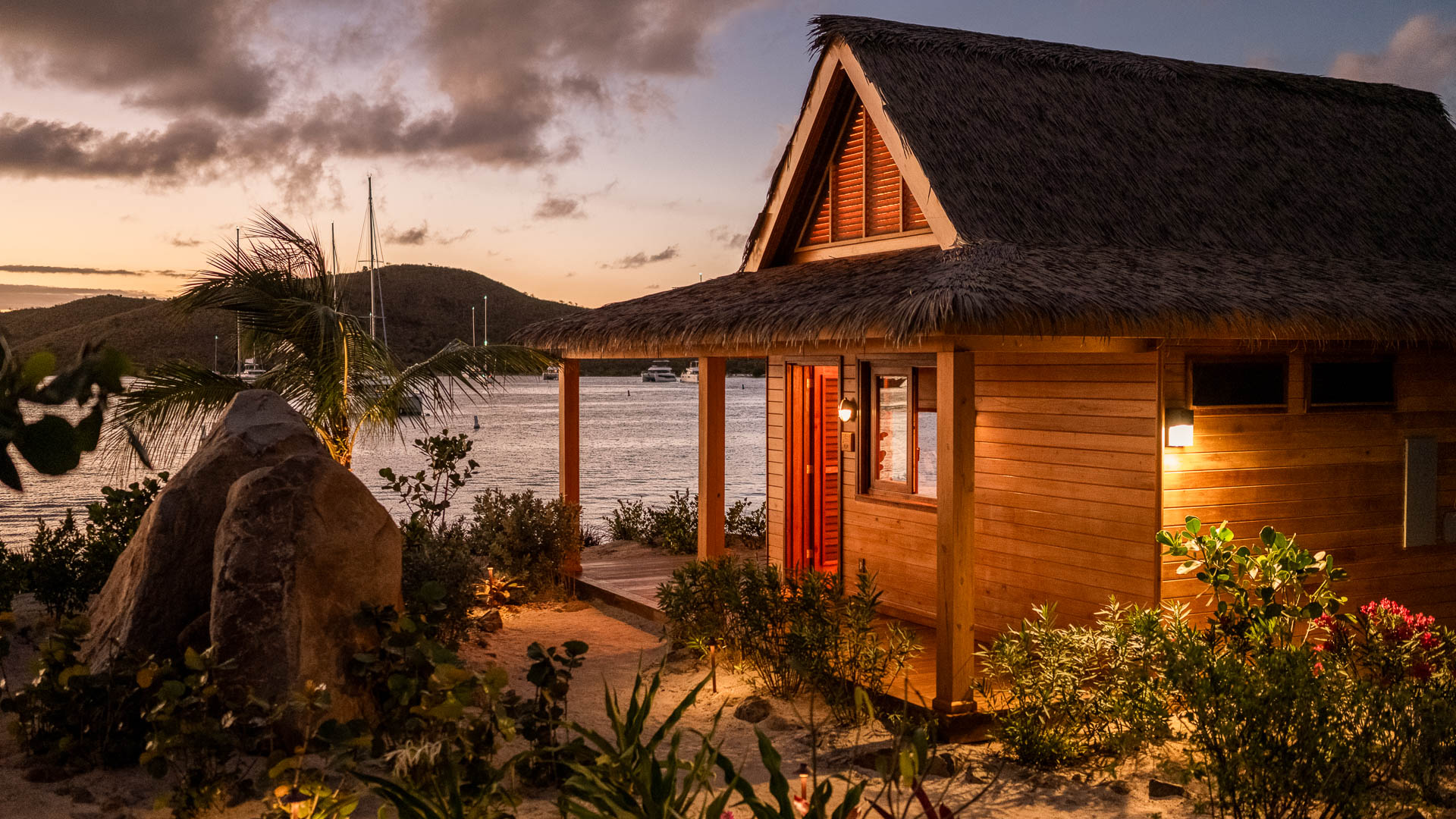 a house with a thatched roof and palm trees next to a body of water