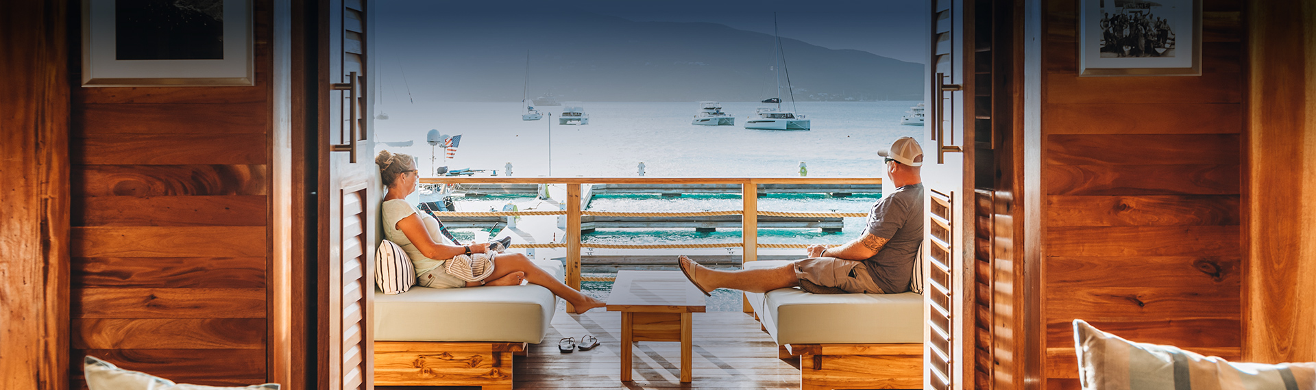 a man and woman lying on couches on a deck overlooking water